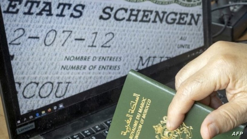A Moroccan man holds his passport in front of his computer displaying a Schengen visa in the capital Rabat, on September 28, 2021. - Paris will sharply reduce the number of visas granted to people from Algeria, Morocco and Tunisia, accusing the former French colonies of not doing enough to allow illegal immigrants to return, a government spokesman said today. (Photo by FADEL SENNA / AFP)