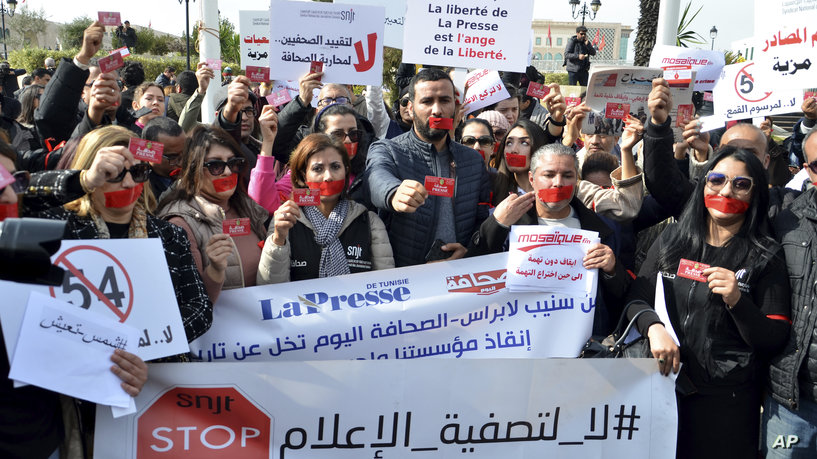 Gaged journalists show their press card as they protest against they say, the danger that threatens the press and the return to dictatorship and a single opinion, especially after the arrest of the general manager of Radio Mosaïque Noureddine Boutar, Thursday, Feb.16, 2023 in Tunis. According to the Journalists Union, the arrest was based on journalistic opinions opposing to Tunisian President Kaies Saied. On banner reads: information is sacred, comment is free. (AP Photo/Hassene Dridi)