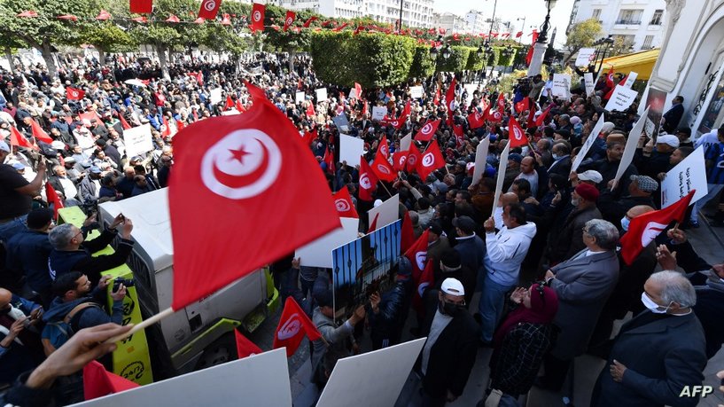 Tunisians raise placards and national flags as they take to the streets of the capital Tunis to protest against their president, on April 10, 2022. - Last July, Tunisian President Kais Saied abruptly suspended the mixed presidential-parliamentary system enshrined in Tunisia's 2014 constitution, a hard-won compromise between rival ideological camps reached three years after a revolt toppled dictator Zine El Abidine Ben Ali. (Photo by FETHI BELAID / AFP)